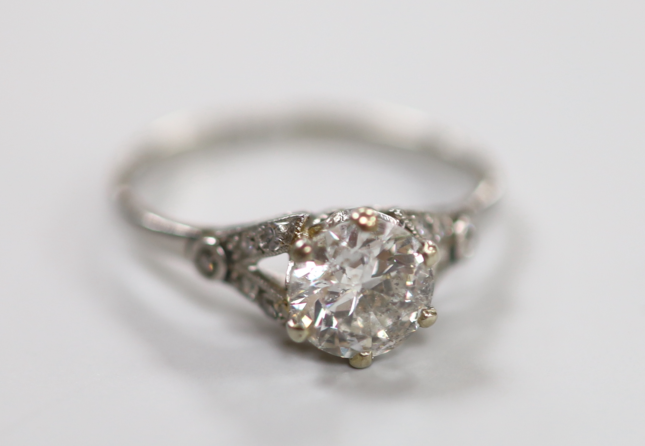 A white metal (stamped plat) and single stone diamond ring, with diamond chip set shoulders, size L/M, gross weight 2.4 grams